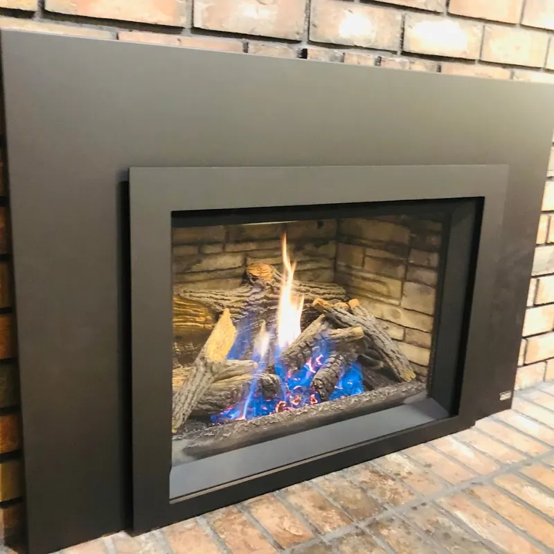 Modern black gas fireplace insert installed in a red brick fireplace, flames lit