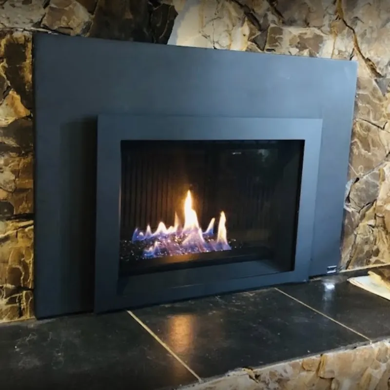 Black gas insert with a wide surround on a natural stone fireplace wall